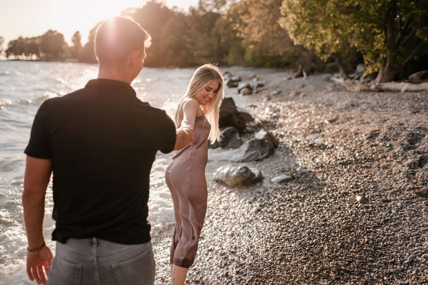 Girl leads man down a beach at golden hour in Kingston, Ontario.