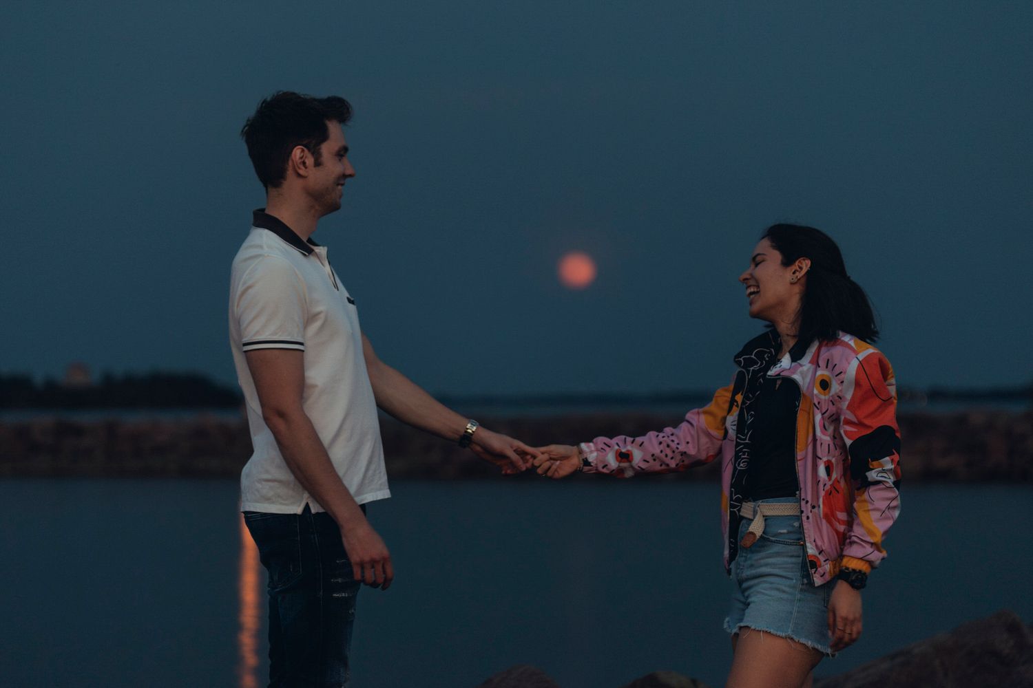 Full moon rises between a couple standing and holding hands in Kingston, Ontario, CA.