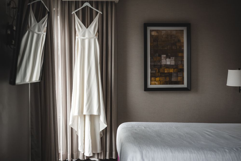 White wedding dress hanging by window with soft natural light in a grey room.