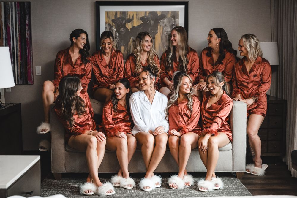 Group wearing matching silk robes sits together on couch during pre-wedding preparations.
