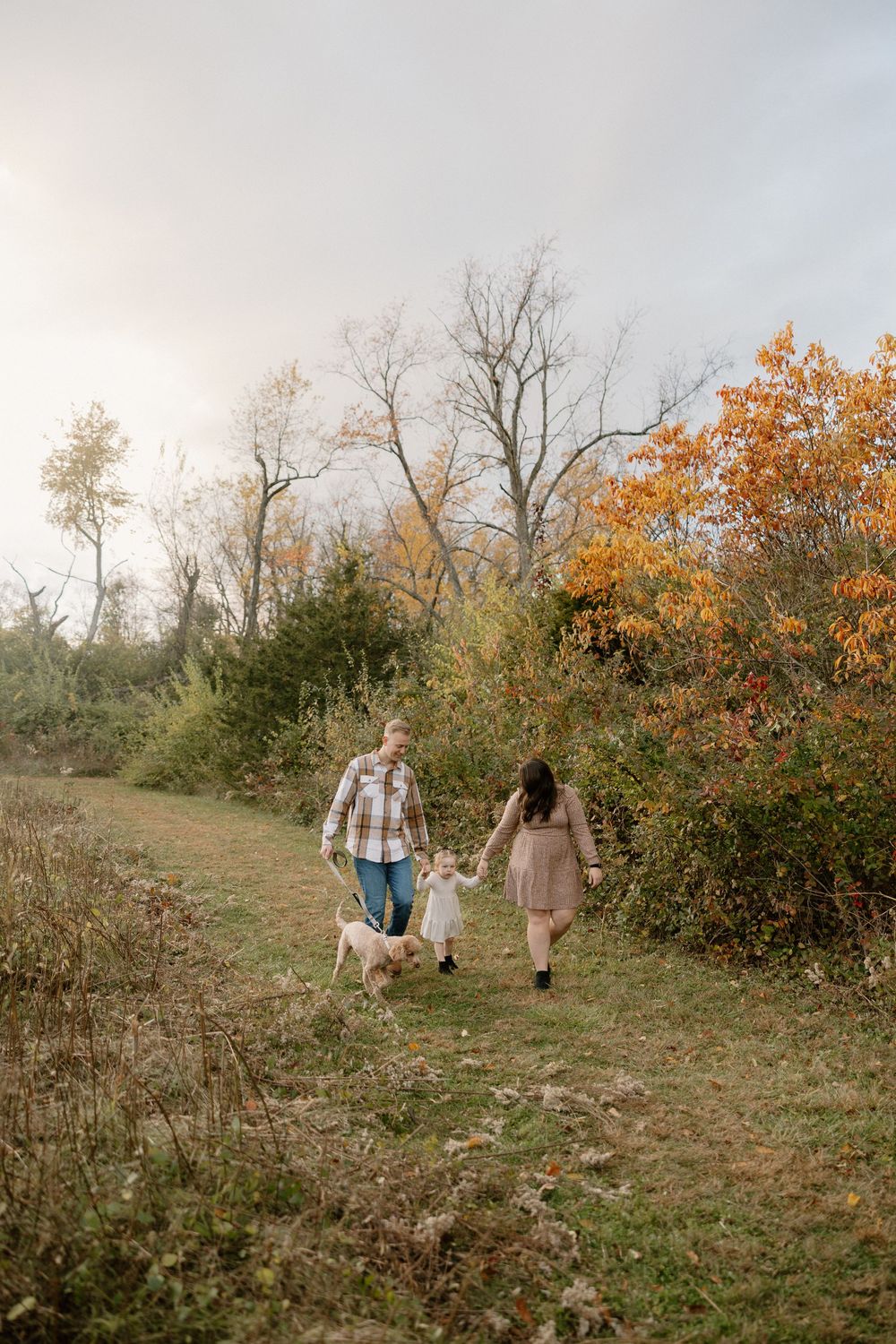 People walking together through a scenic autumn hillside with orange foliage and bare trees in the background.