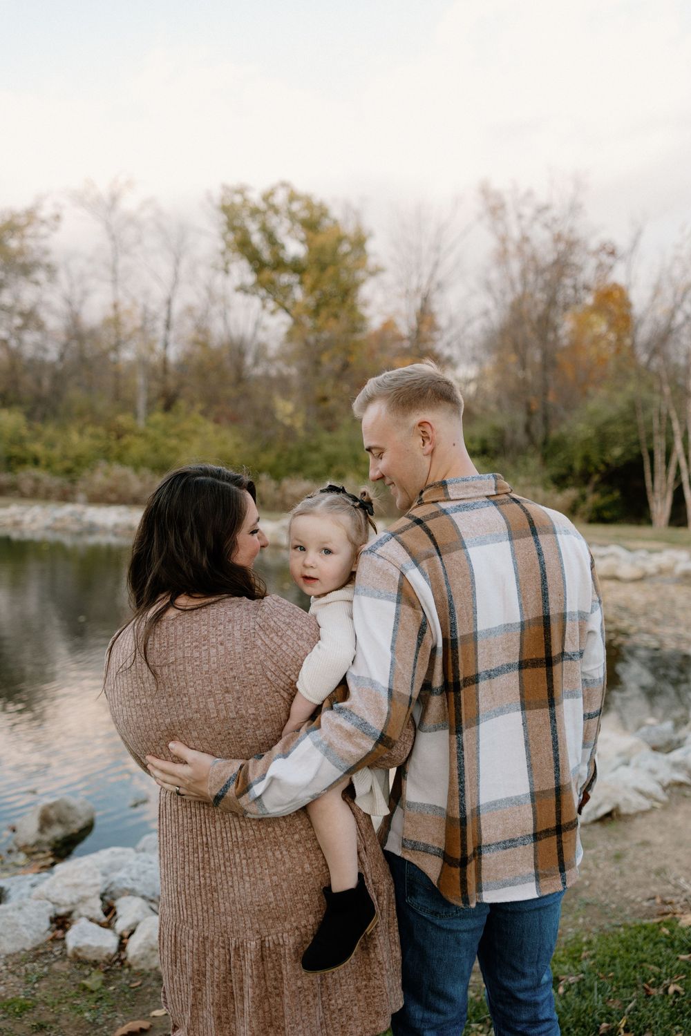 A family shares an intimate moment by a serene lake during an autumn photoshoot in nature.
