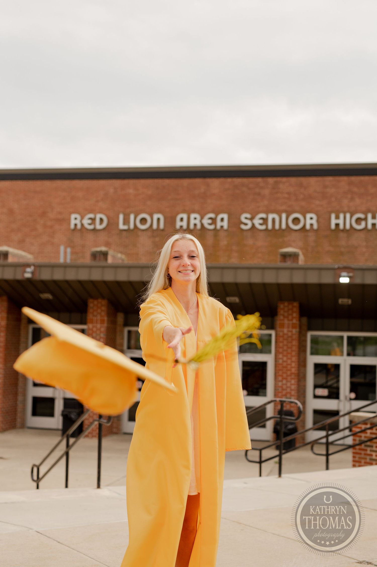 Graduate in bright yellow cap and gown posing in front of Red Lion Area Senior High School entrance.
