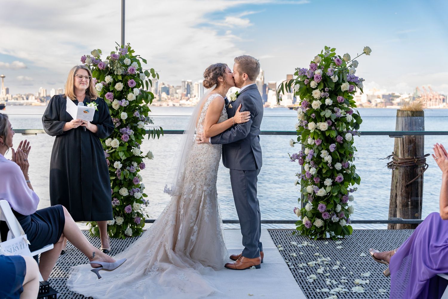 A romantic waterfront wedding ceremony with floral columns and a veil flowing in the breeze on a marina dock.