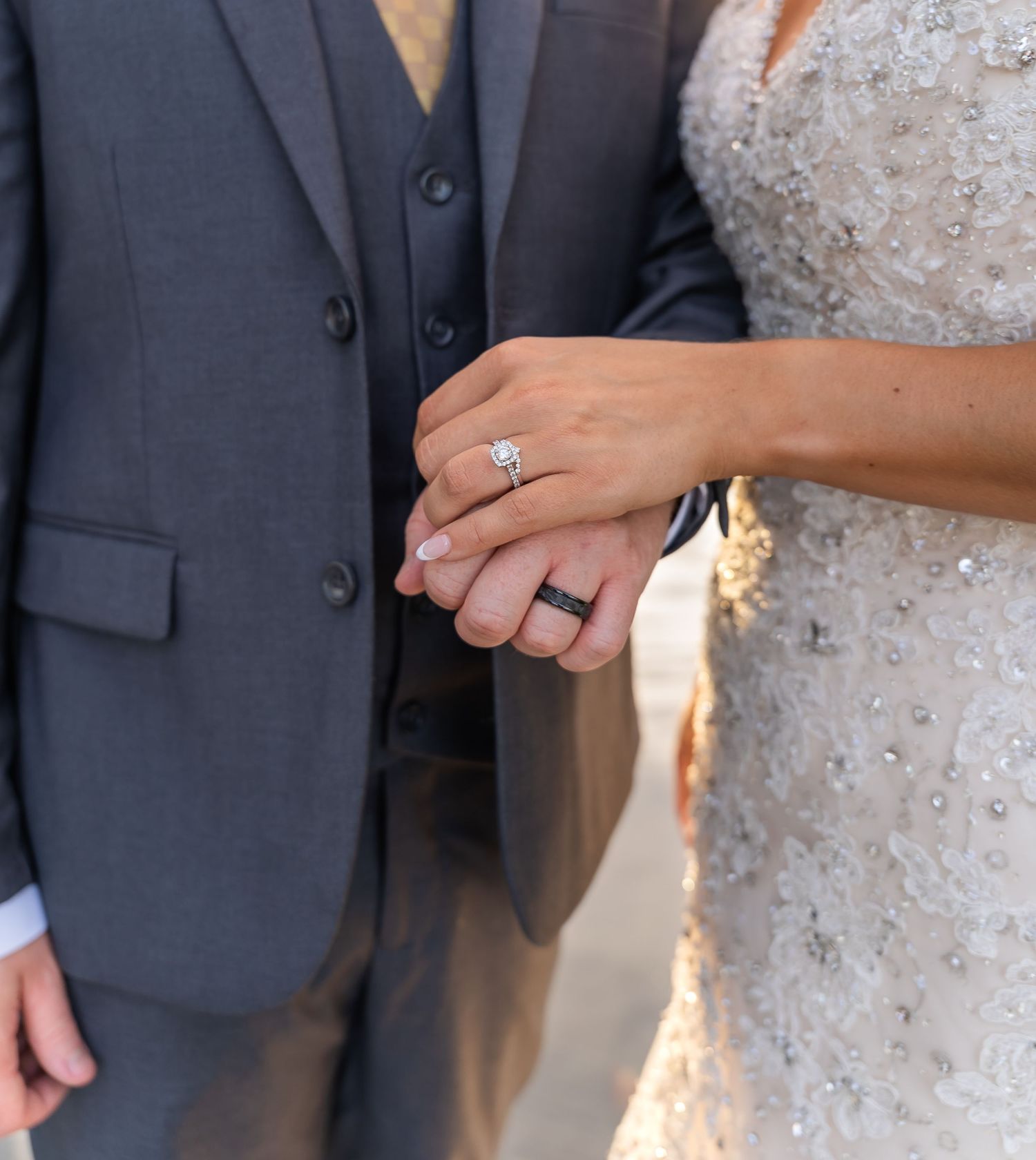 Close-up of newly married couple's hands showing wedding rings and engagement ring against formal attire.