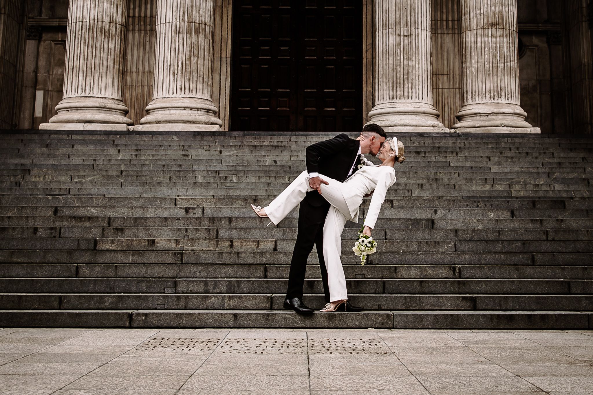 Couple posing on grand stone steps with classical columns in the background.