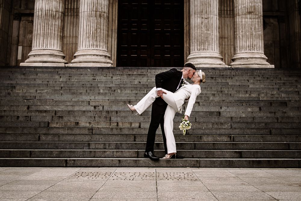 Couple posing on grand stone steps with classical columns in the background.