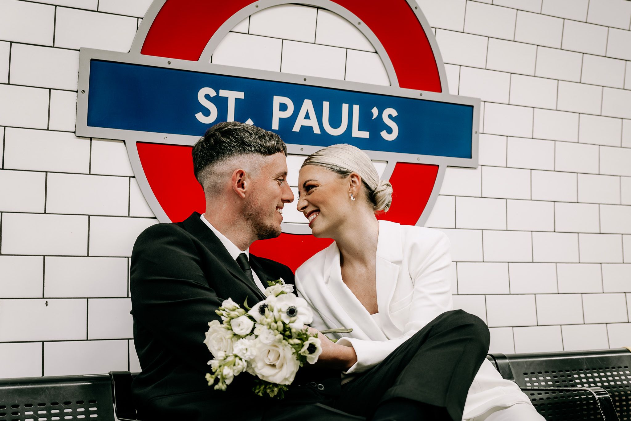 Couple poses for wedding photos at St Paul's London Underground station with iconic red roundel.