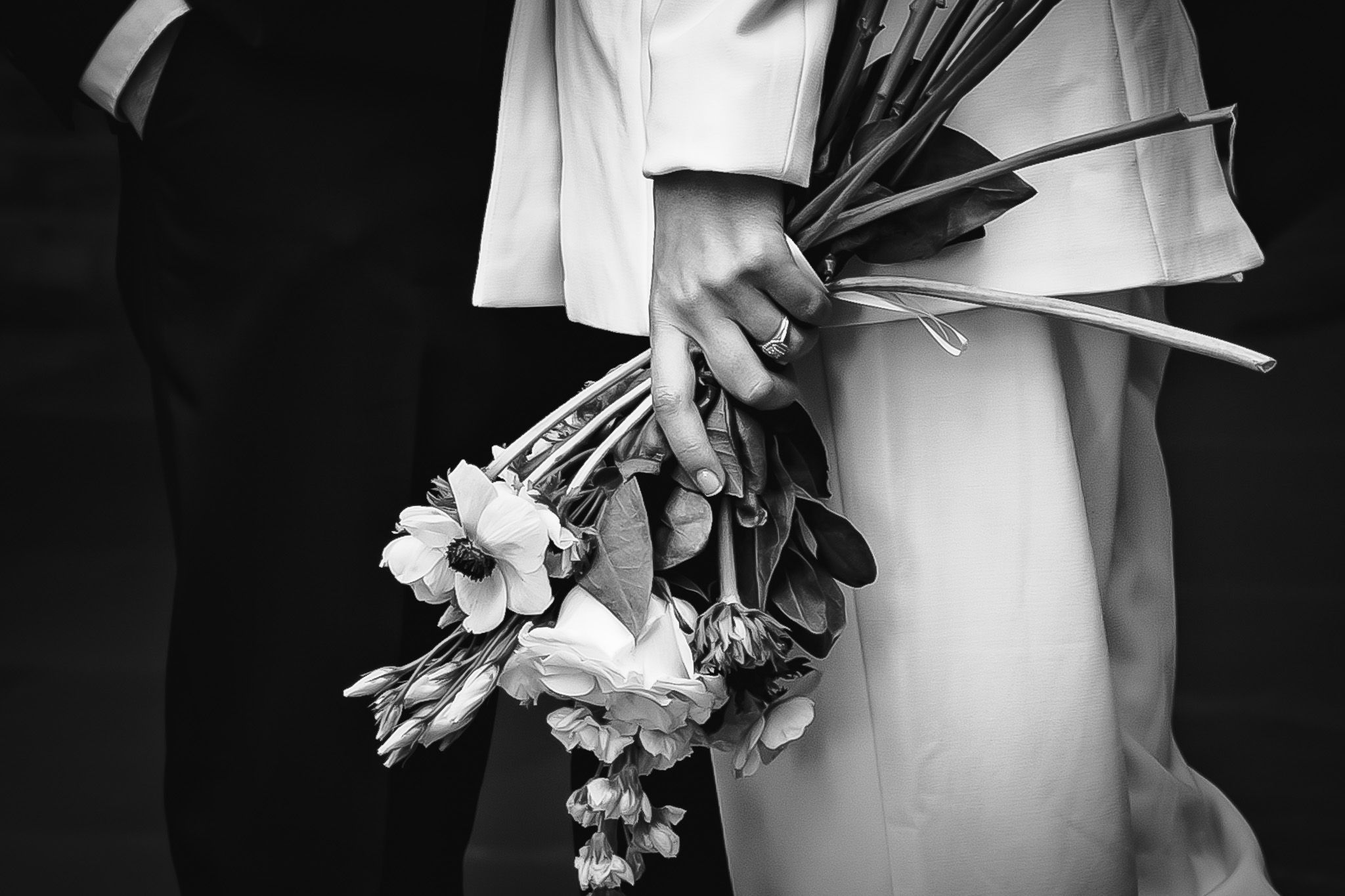 Wedding party member holding white floral bouquet against dark background.