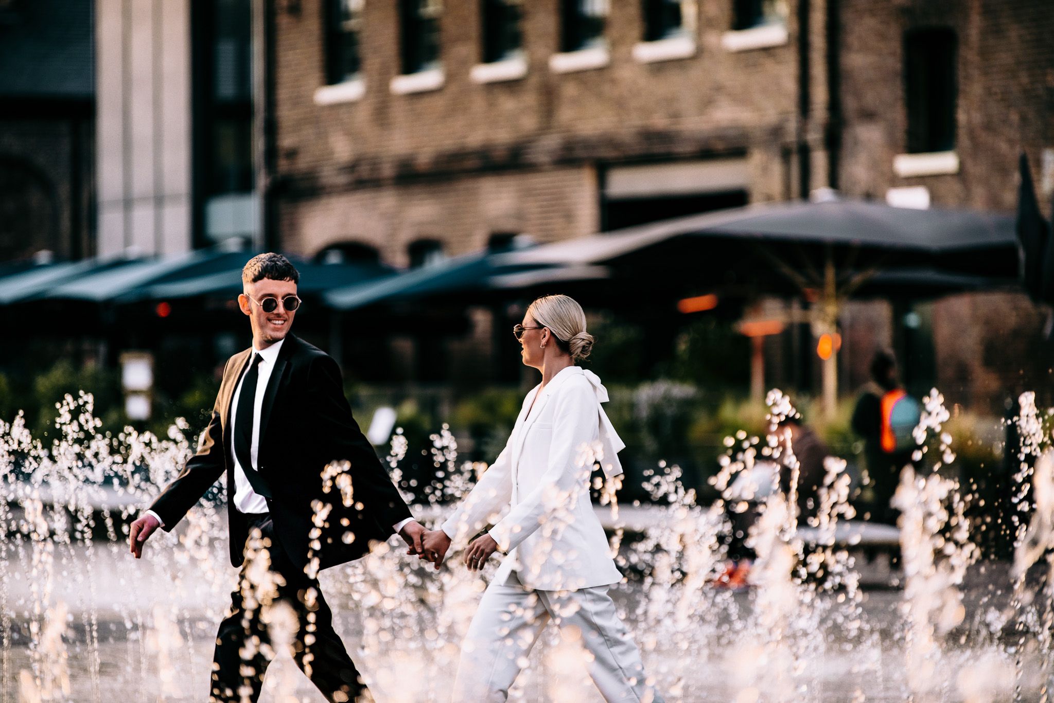 Wedding couple walking near urban water fountains spraying in the background.