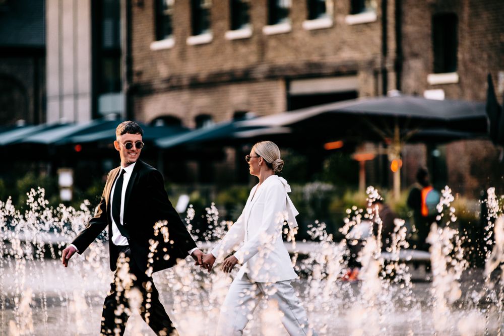 Wedding couple walking near urban water fountains spraying in the background.