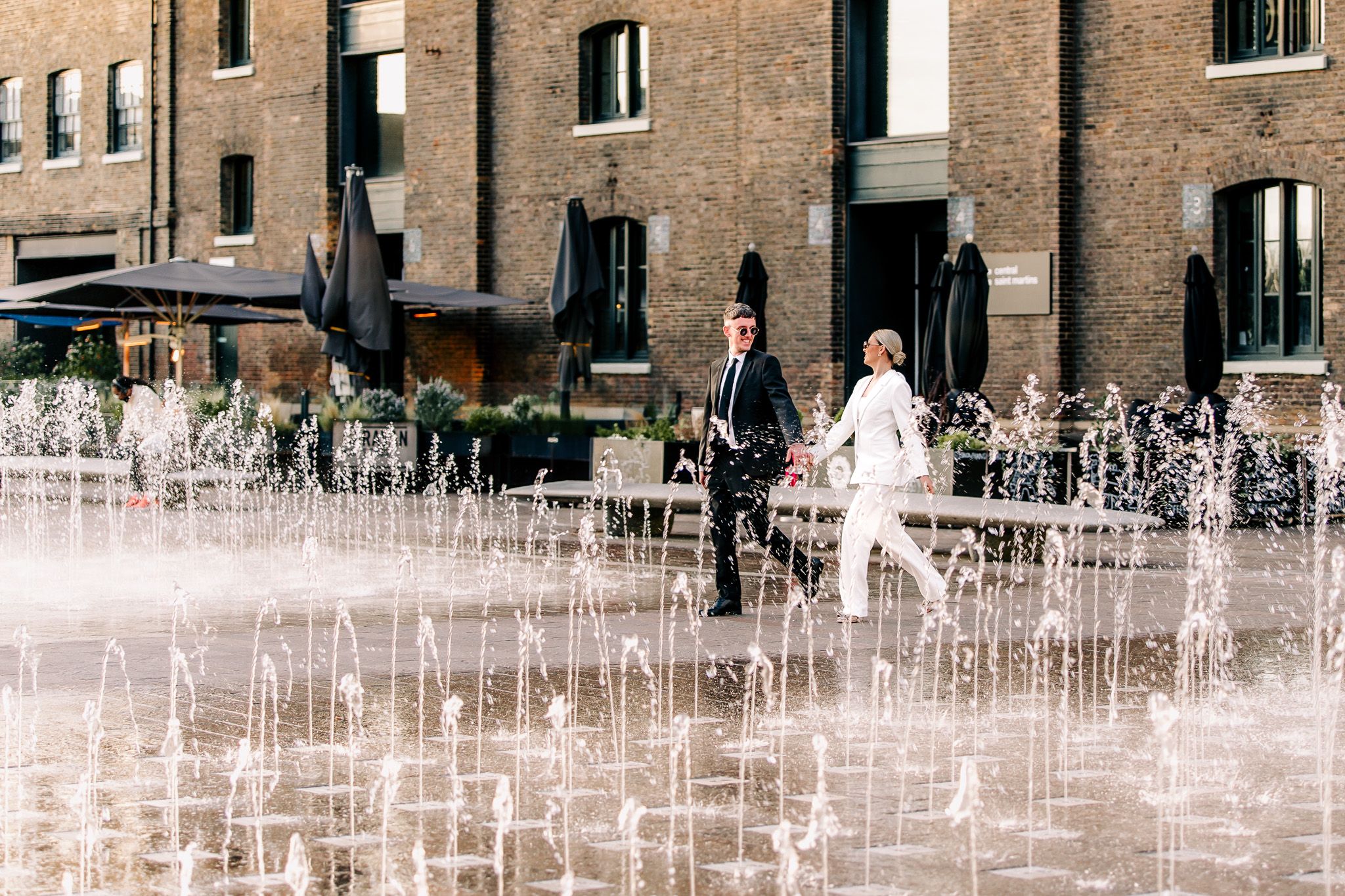 Water fountain display creates geometric patterns in front of brick building.