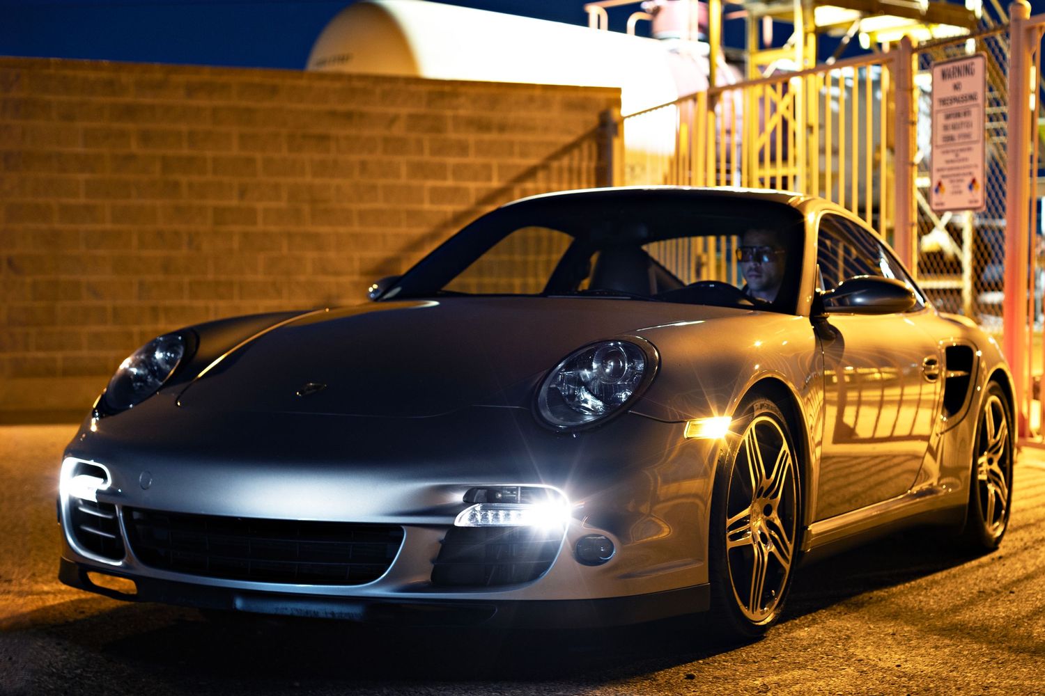 Silver Porsche 911 sports car illuminated at night against brick building.