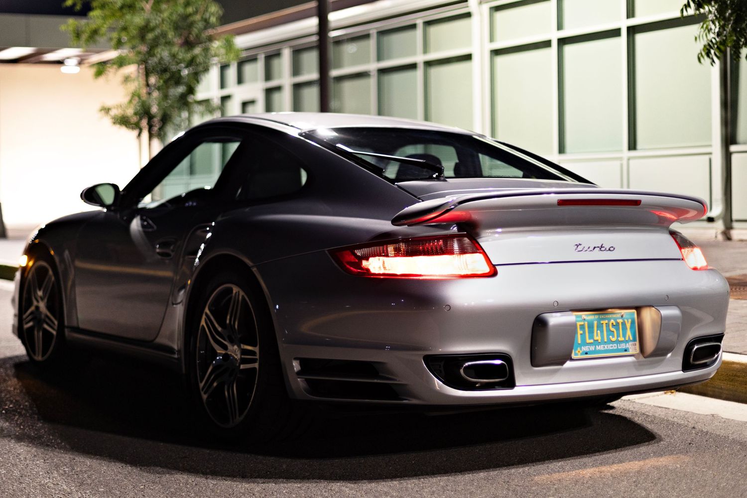 Rear view of silver Porsche 911 Turbo parked at night showing distinctive taillights.