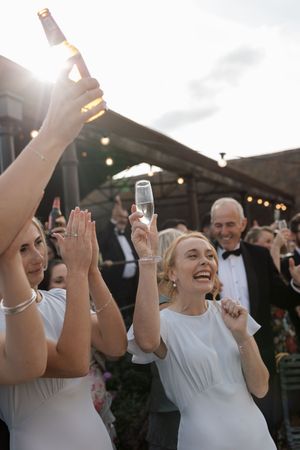 Wedding guests raise their glasses in celebration at an outdoor reception under string lights.