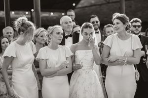 Wedding party members in white dresses share candid laughs during an outdoor celebration.