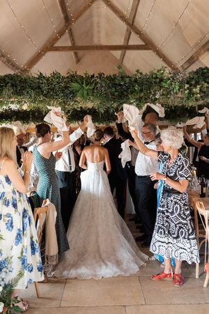 Wedding guests dance together under a tent with floral decorations and a white ballgown dress visible.