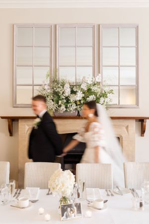 Elegant wedding reception table with white floral centerpiece and window panels in background.