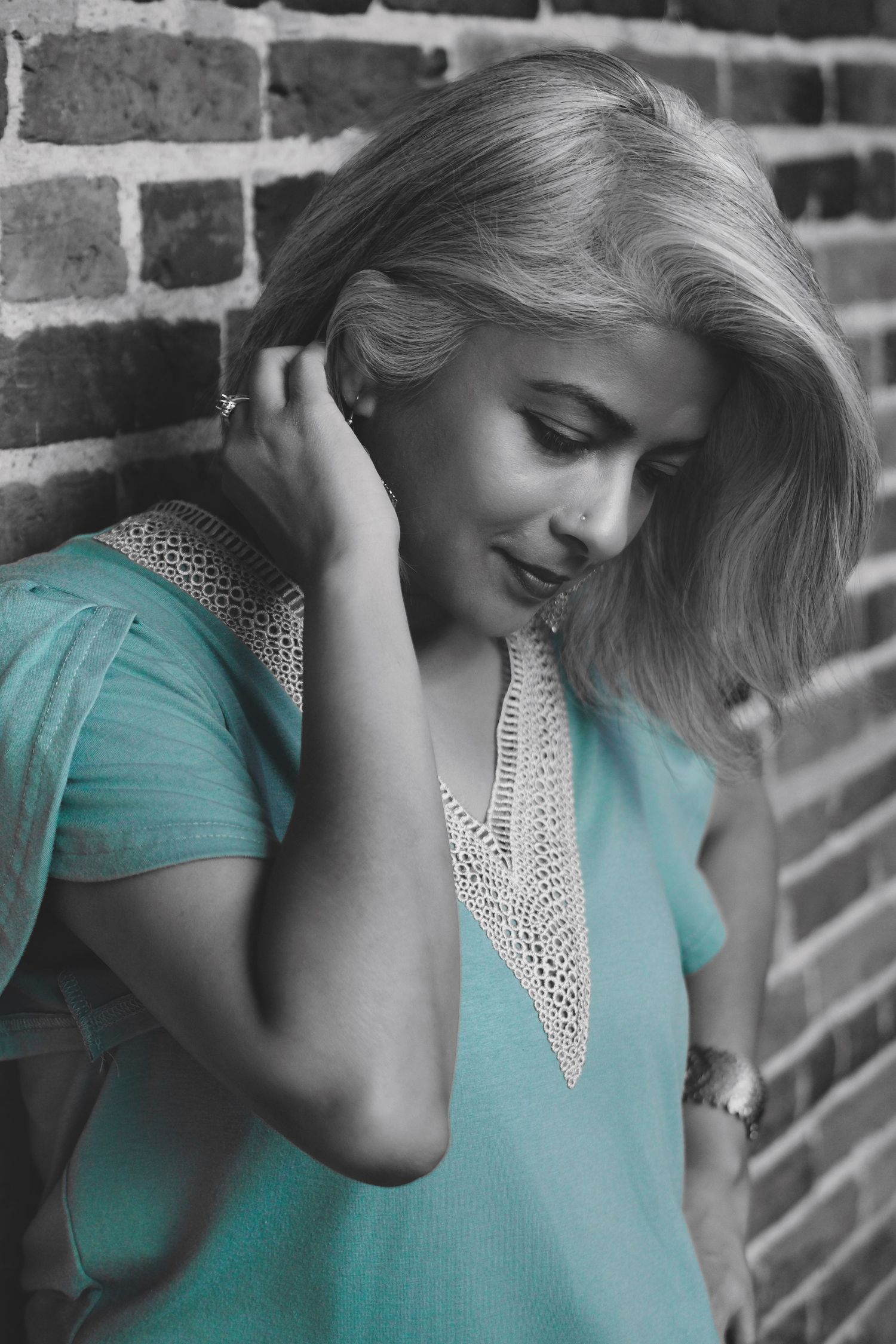 Portrait in turquoise top leaning against brick wall with selective color treatment.