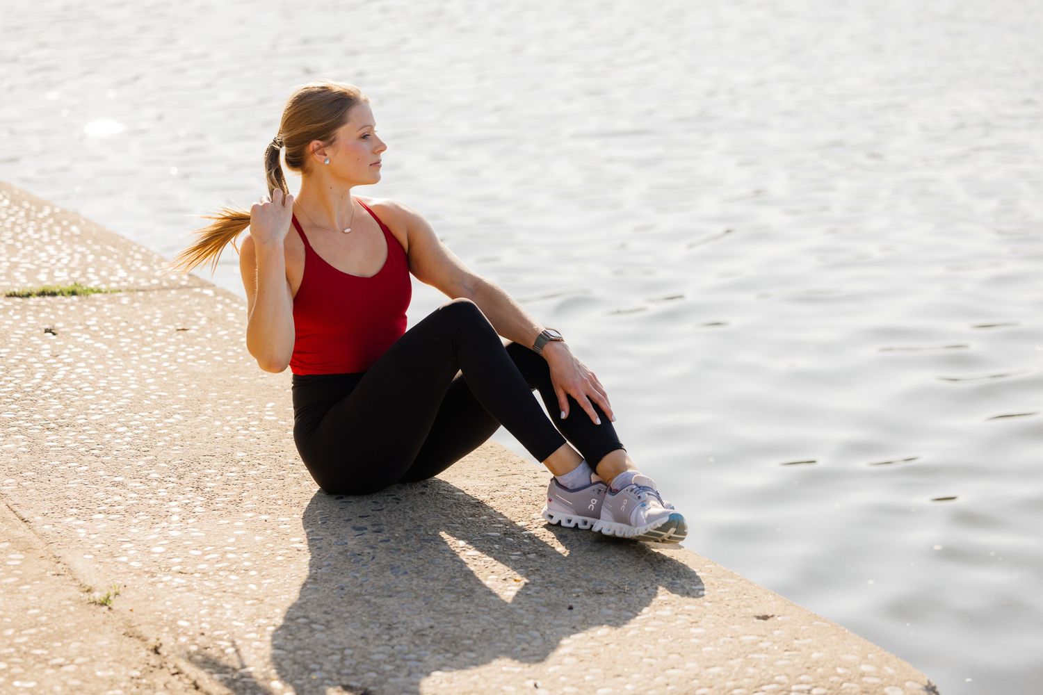 Person in red tank top resting by waterfront on sunny day.