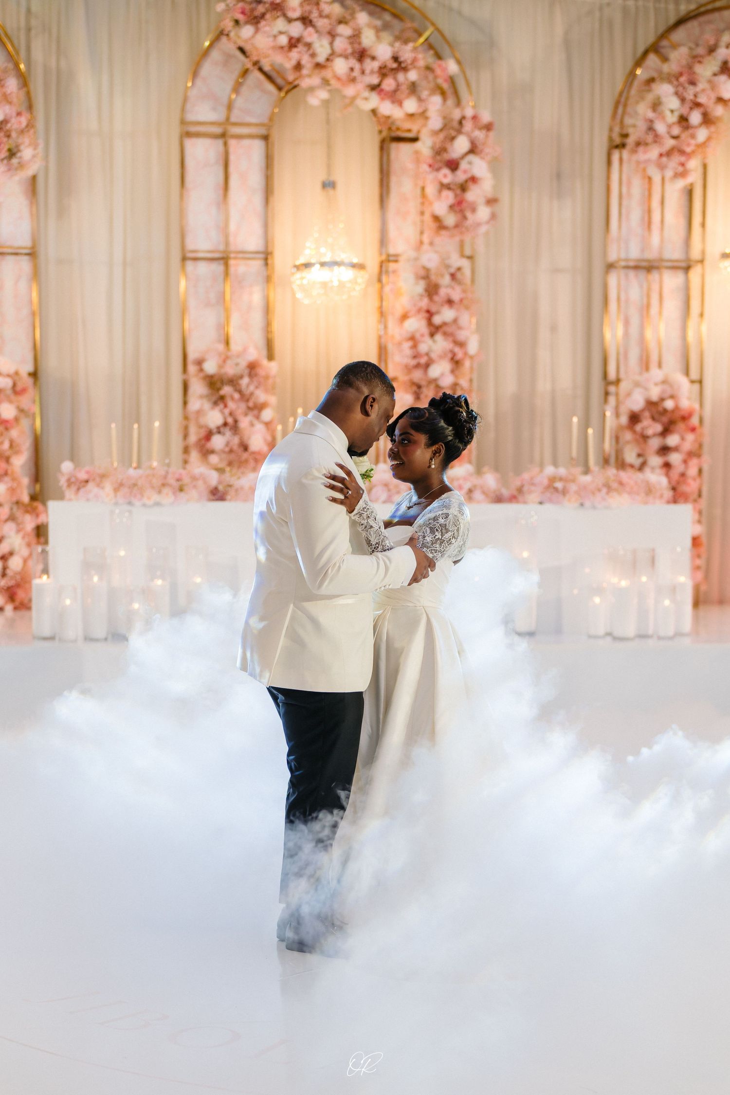 Romantic first dance moment with couple surrounded by pink floral arches and fog effect.