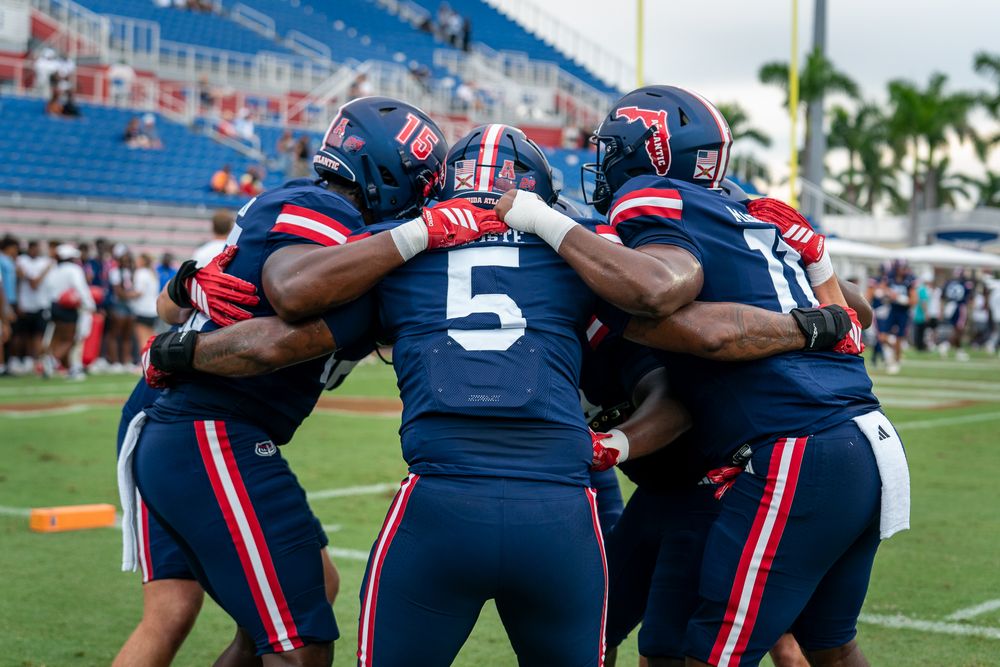 FAU college football game action under stadium lights, players clashing on the field, high-energy sports photo by SRX Media Group