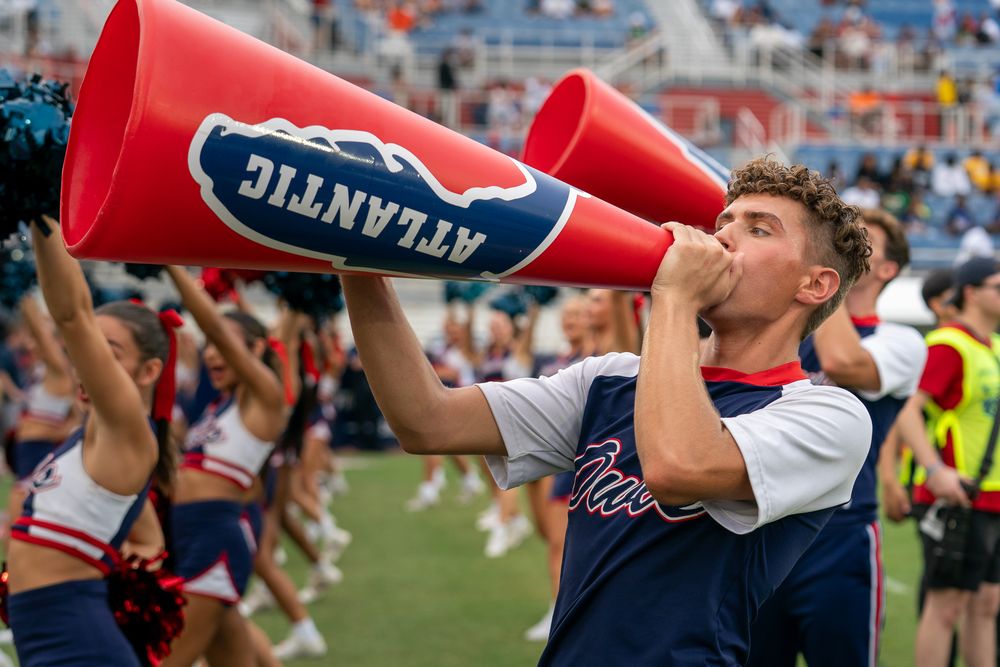 FAU college football game action under stadium lights, players clashing on the field, high-energy sports photo by SRX Media Group