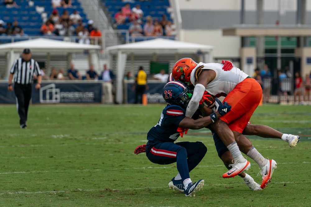 FAU college football game action under stadium lights, players clashing on the field, high-energy sports photo by SRX Media Group