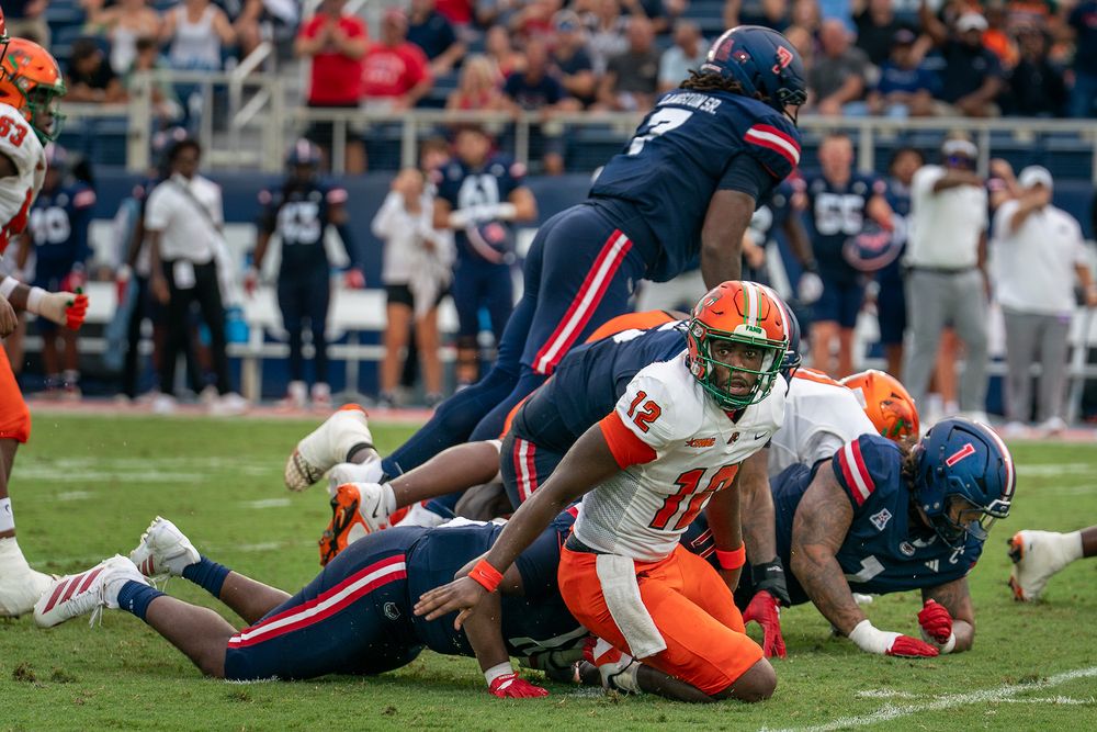 FAU college football game action under stadium lights, players clashing on the field, high-energy sports photo by SRX Media Group