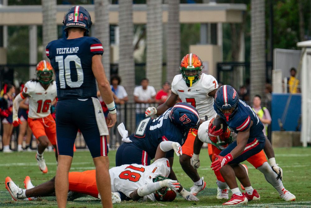 FAU college football game action under stadium lights, players clashing on the field, high-energy sports photo by SRX Media Group