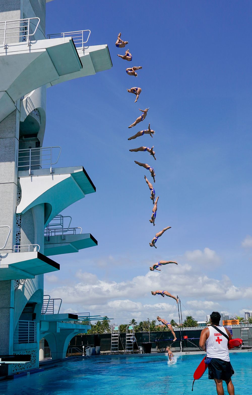 High diver in midair against a clear blue sky, captured as they leap from a diving platform during a sports and leisure photography