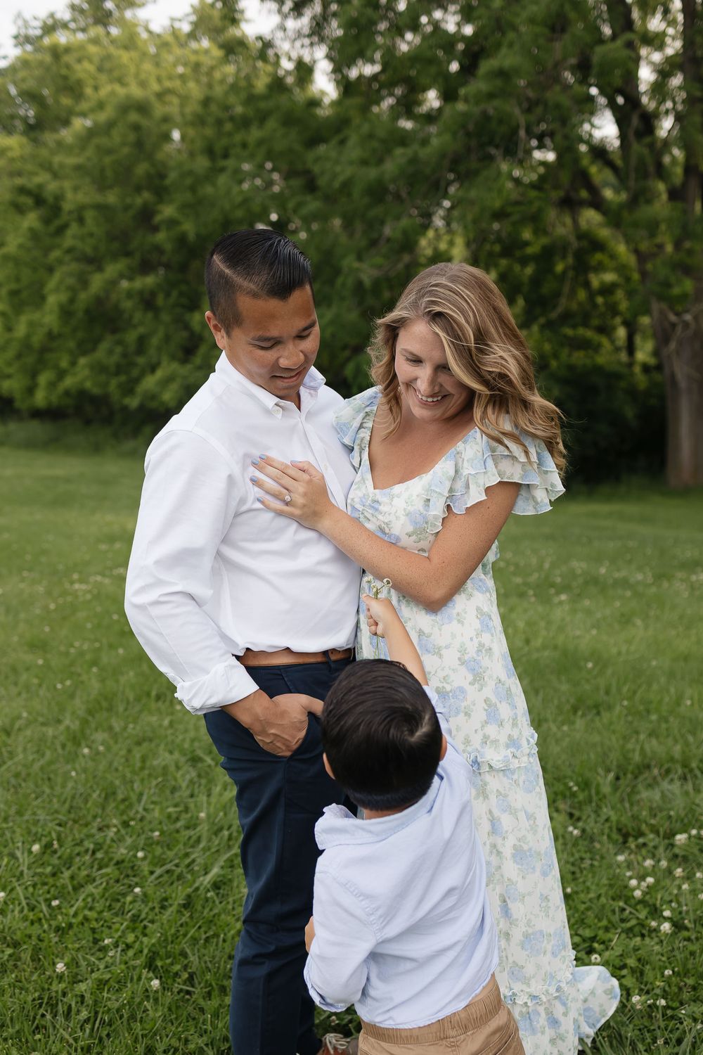 son handing picked flower to mom and dad snuggled close Family photographers kansas city