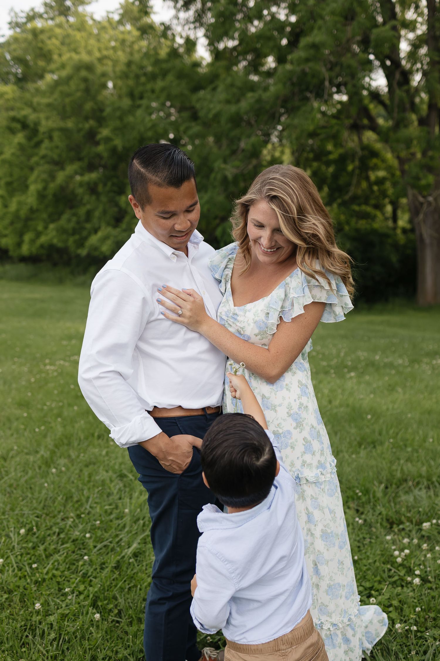 son handing picked flower to mom and dad snuggled close Family photographers kansas city
