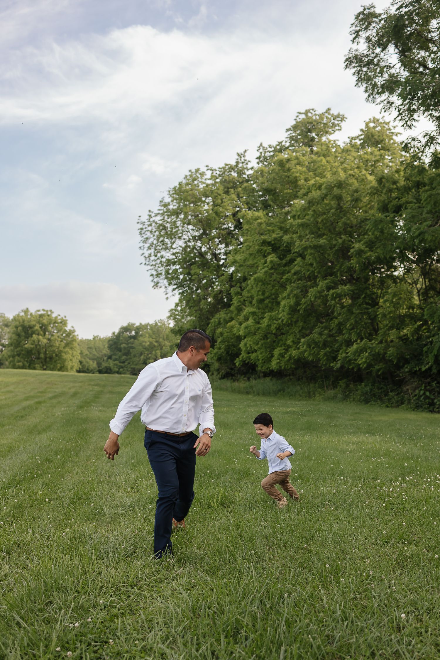 dad and son playing tag in an open field with beautiful blue skies Family photographers kansas city