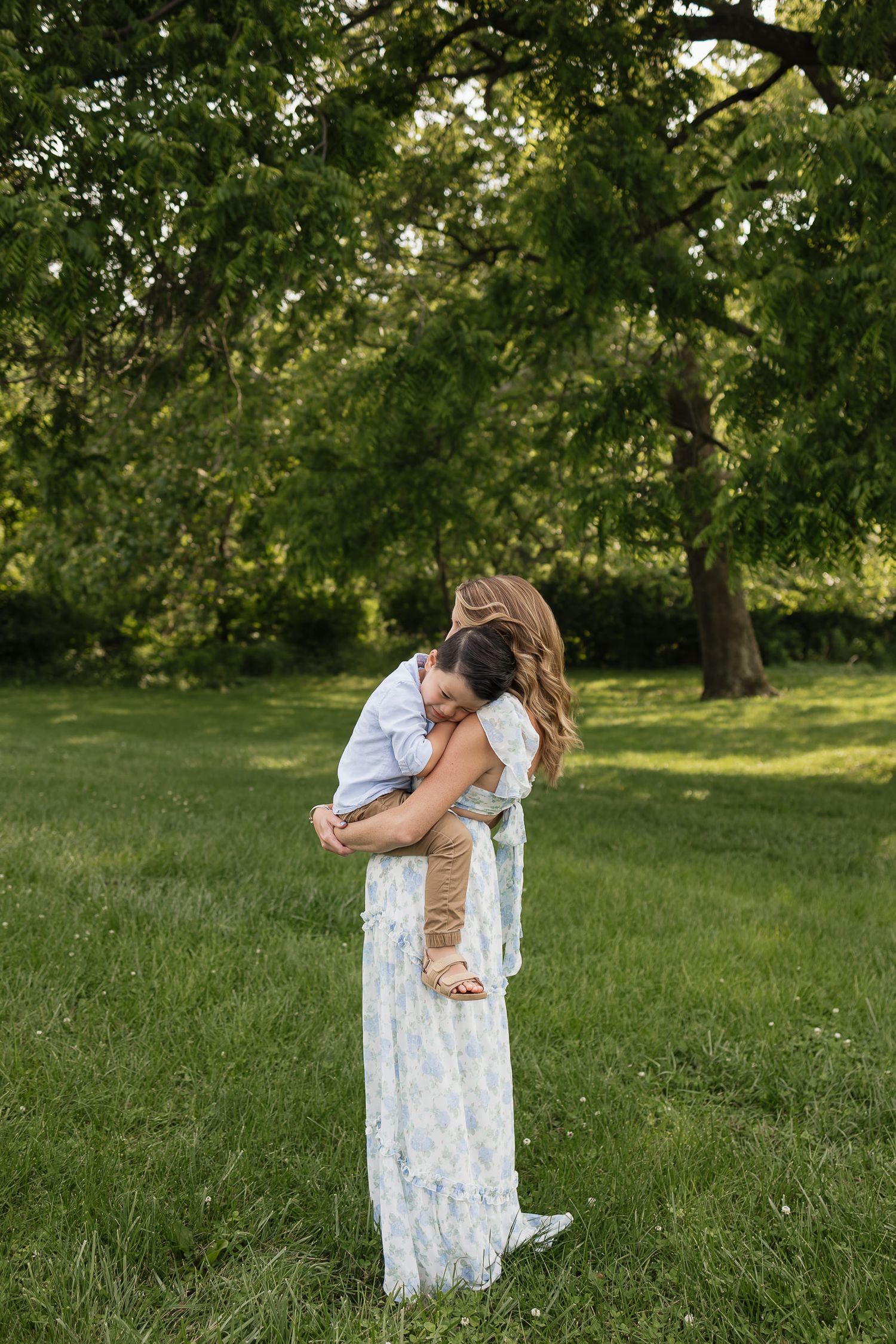 son resting on moms shoulder as she holds him in blue and white floral dress Family photographers kansas city