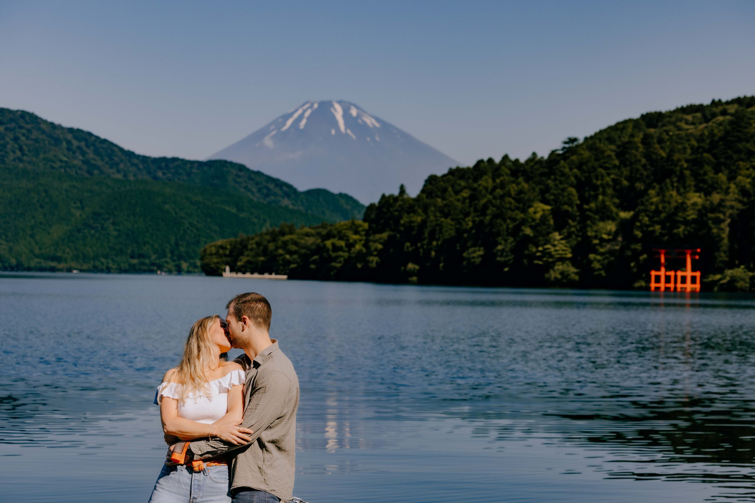 A tranquil scene at Lake Ashi with Mount Fuji rising majestically in the background and a red torii gate visible on the water.