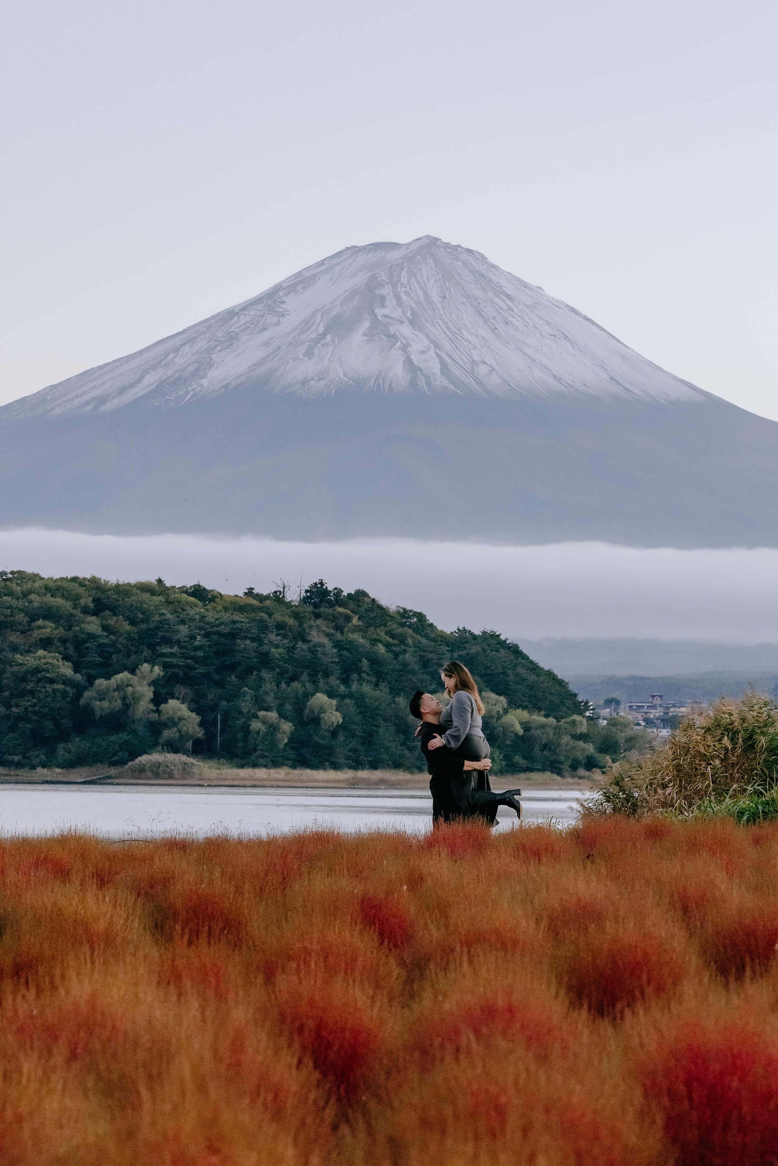 Mount Fuji rises majestically above autumn landscape with red grass and foggy conditions in Japan.