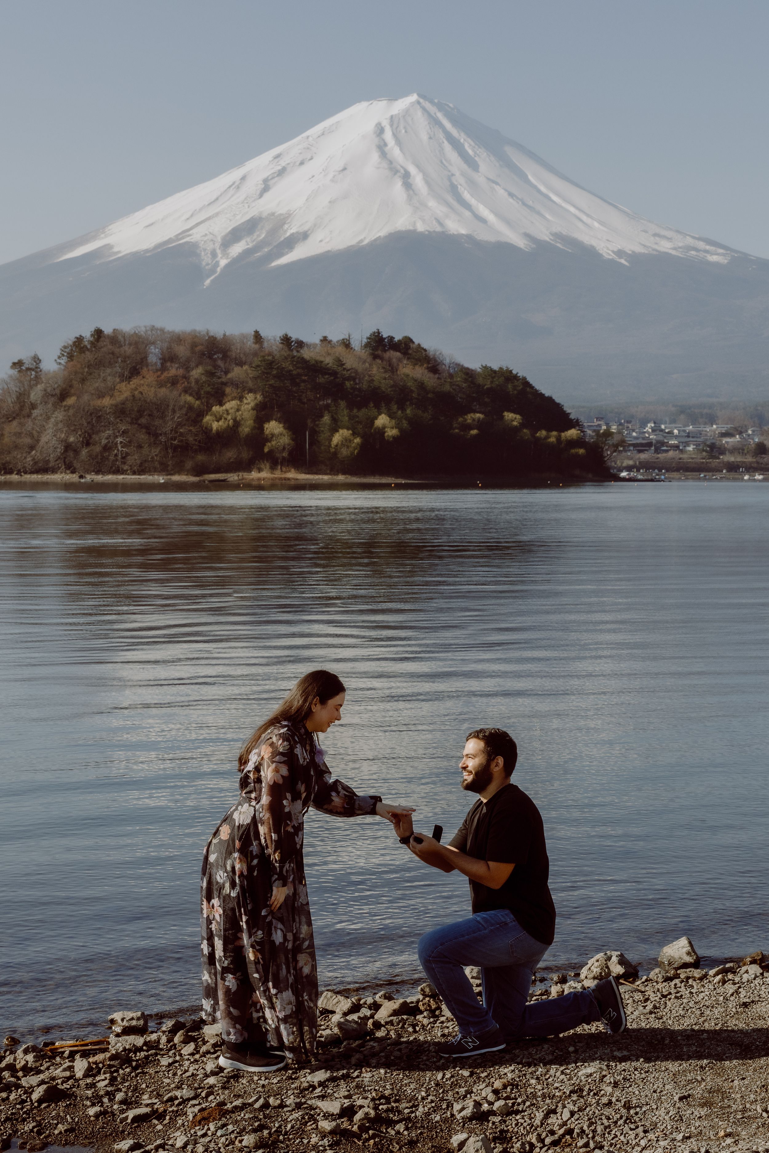 A romantic proposal scene takes place on the shores of Lake Kawaguchiko with Mount Fuji rising majestically in the background.