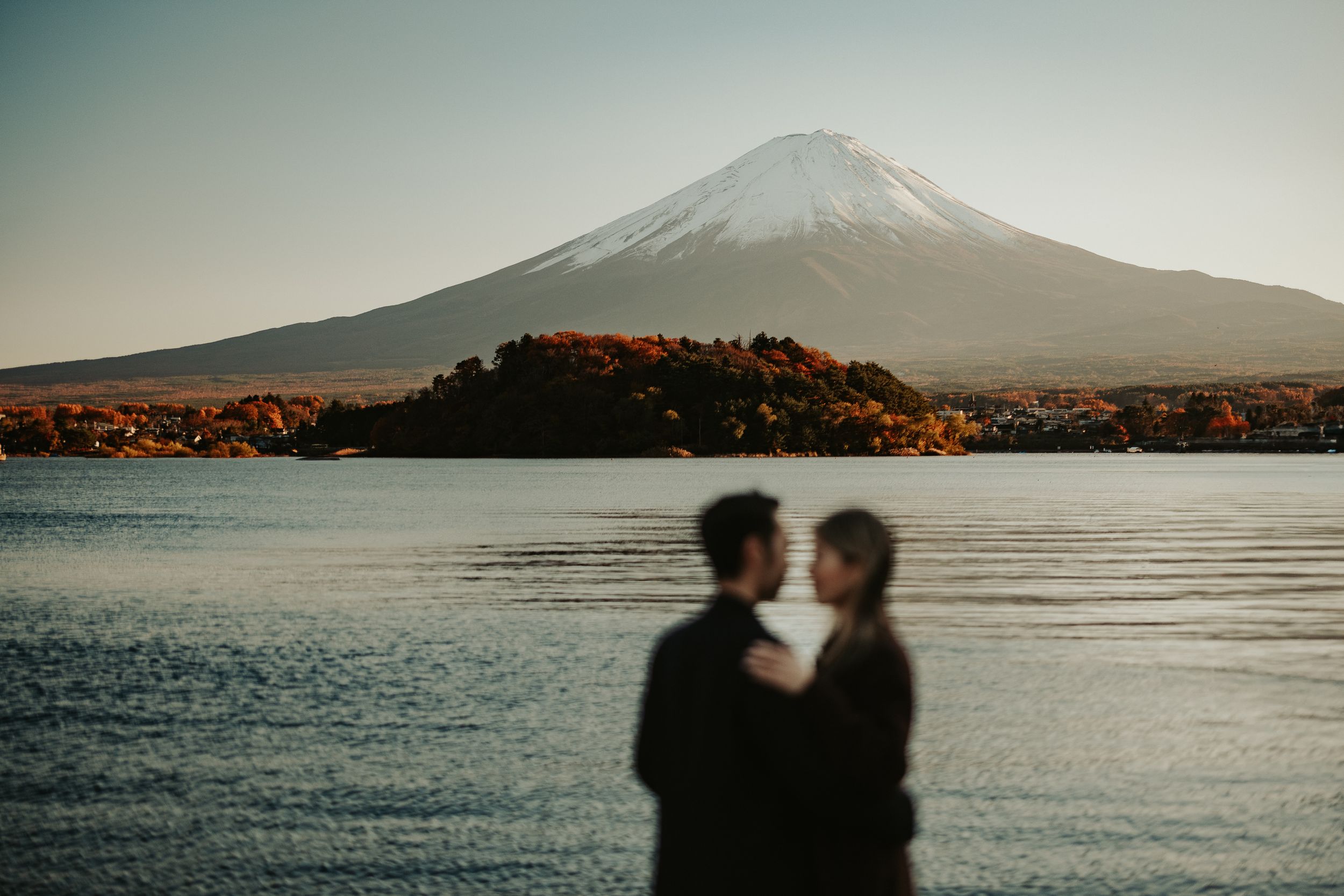 Silhouetted figures stand against the backdrop of Mount Fuji during golden hour at Lake Kawaguchiko.