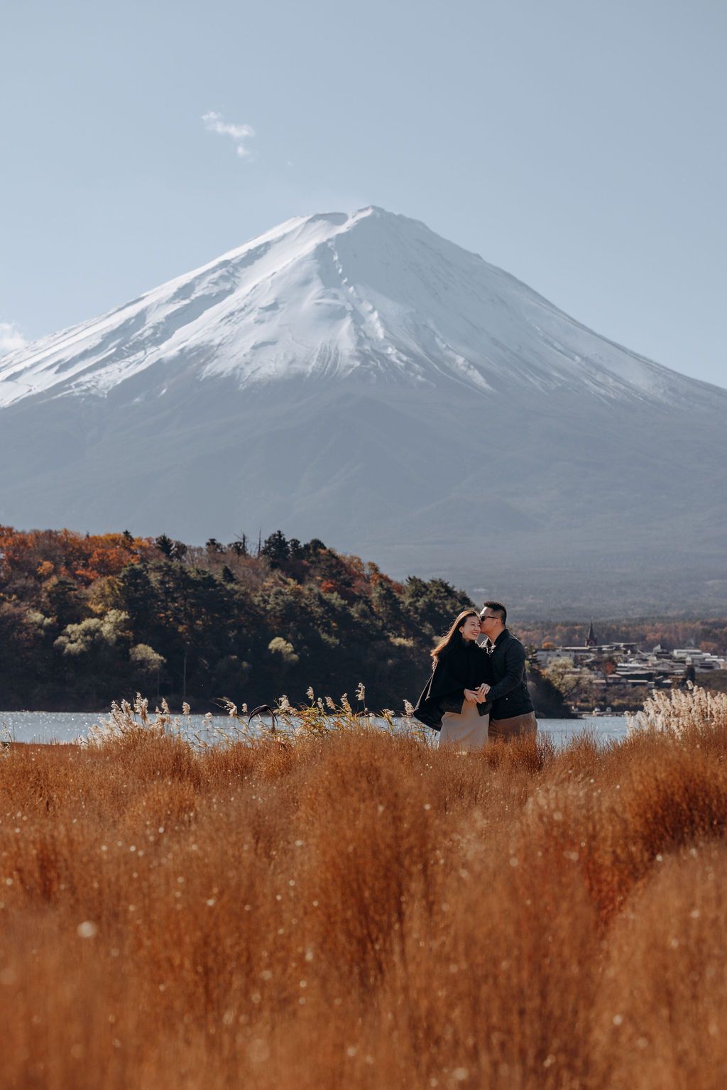 Mount Fuji rises majestically over a lake with golden autumn grass in the foreground on a clear day in Japan.