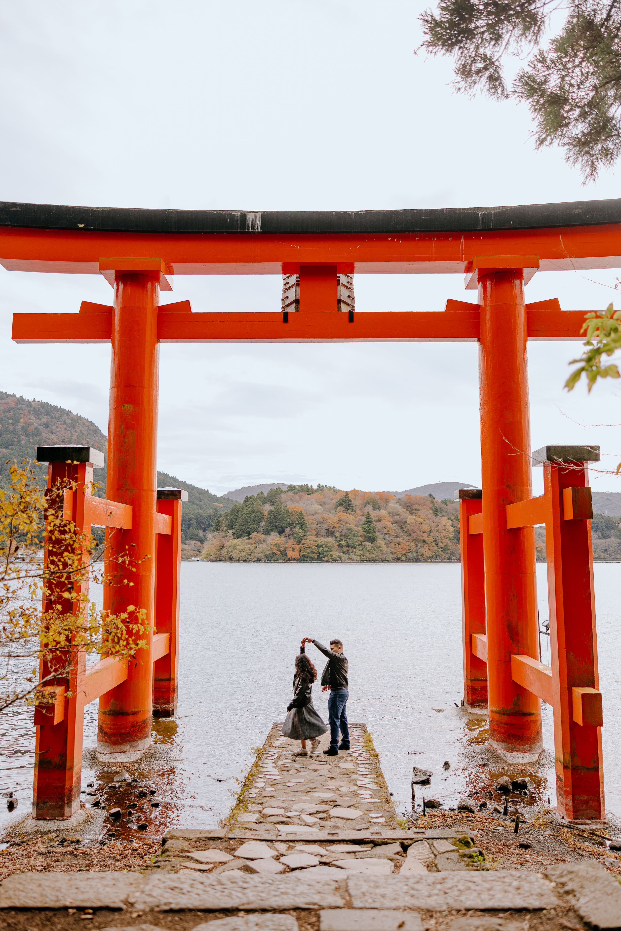 A series of bright orange torii gates frame a peaceful lake view at a Japanese shrine during autumn.