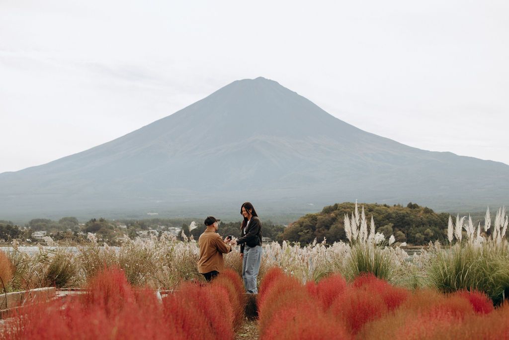 Two people stand in a field of red grasses and pampas grass with Mount Fuji rising majestically in the background.