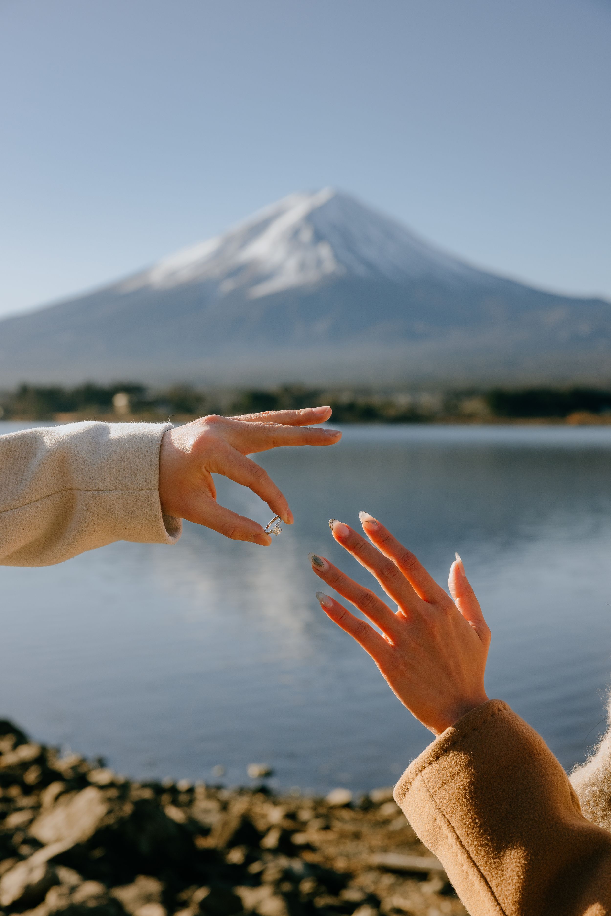 Hands reach out to frame Mount Fuji across Lake Kawaguchiko in Japan during a clear sunny day.