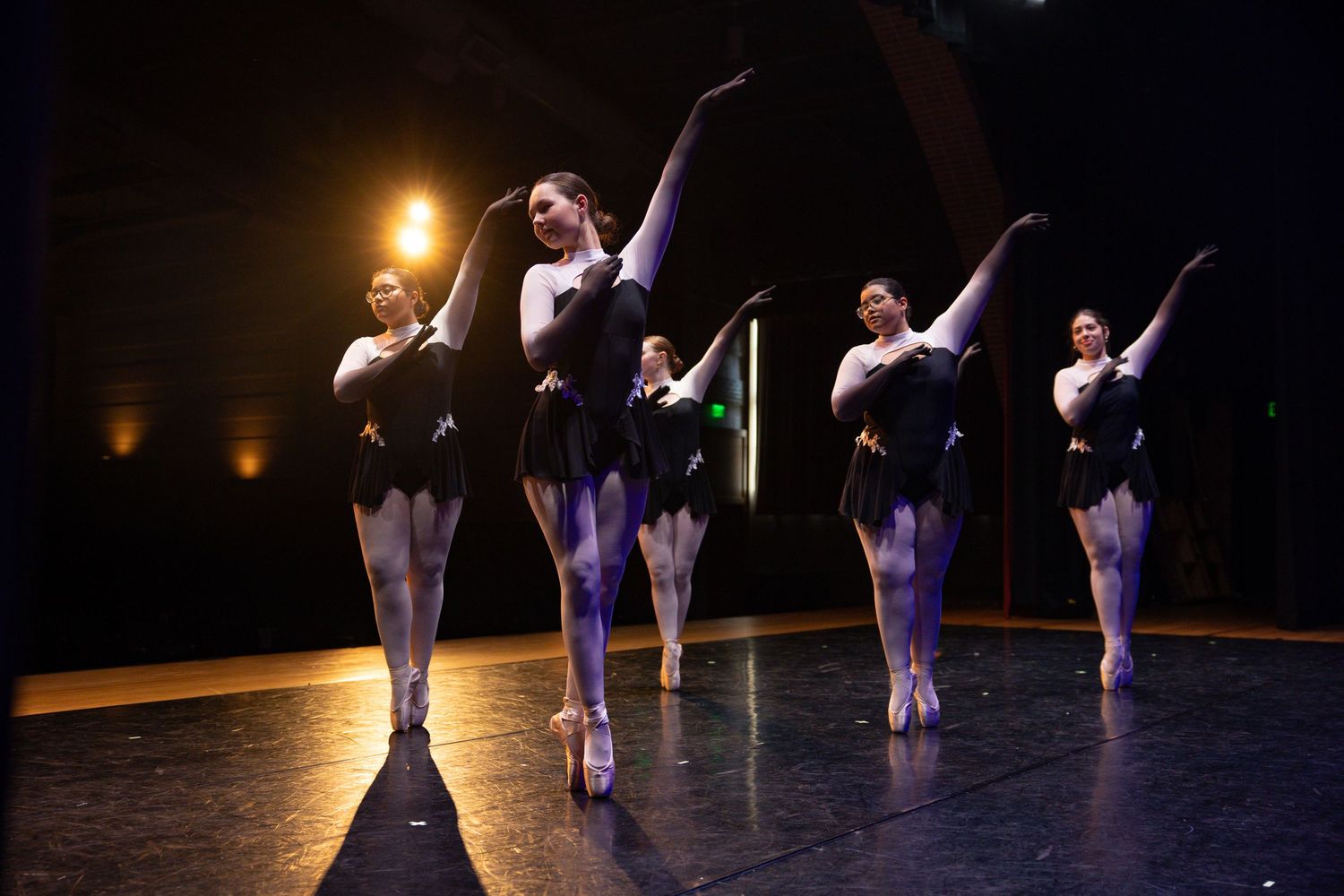 Ballet dancers in traditional tutus perform on dimly lit stage with spotlight effect.