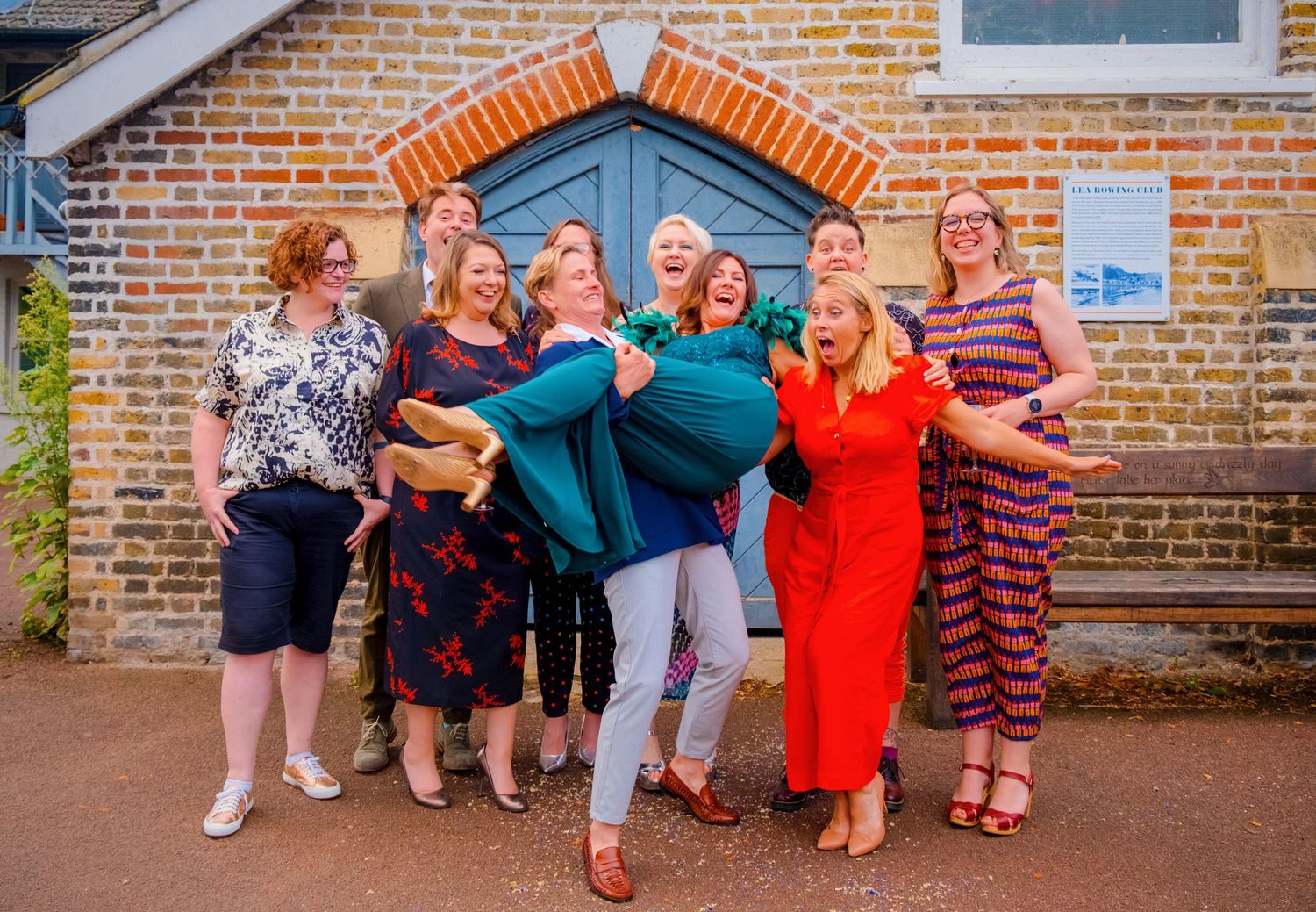Playful group photo of friends posing together in colorful dresses against a brick building.