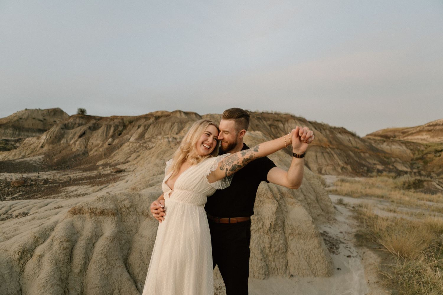 A couple shares an intimate moment against dramatic badlands landscape at sunset.