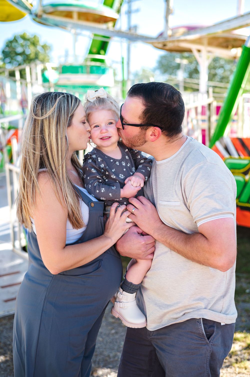 Family sharing tender moments at a colorful carnival with rides in the background.