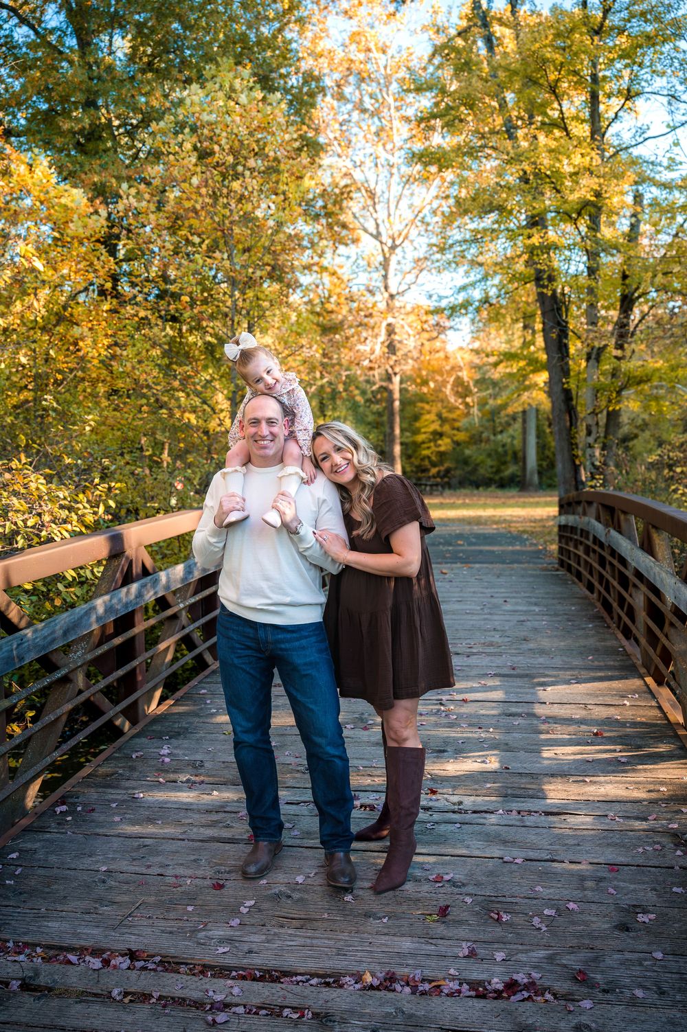 Three candid moments captured on a wooden bridge surrounded by autumn trees with golden foliage in the background.