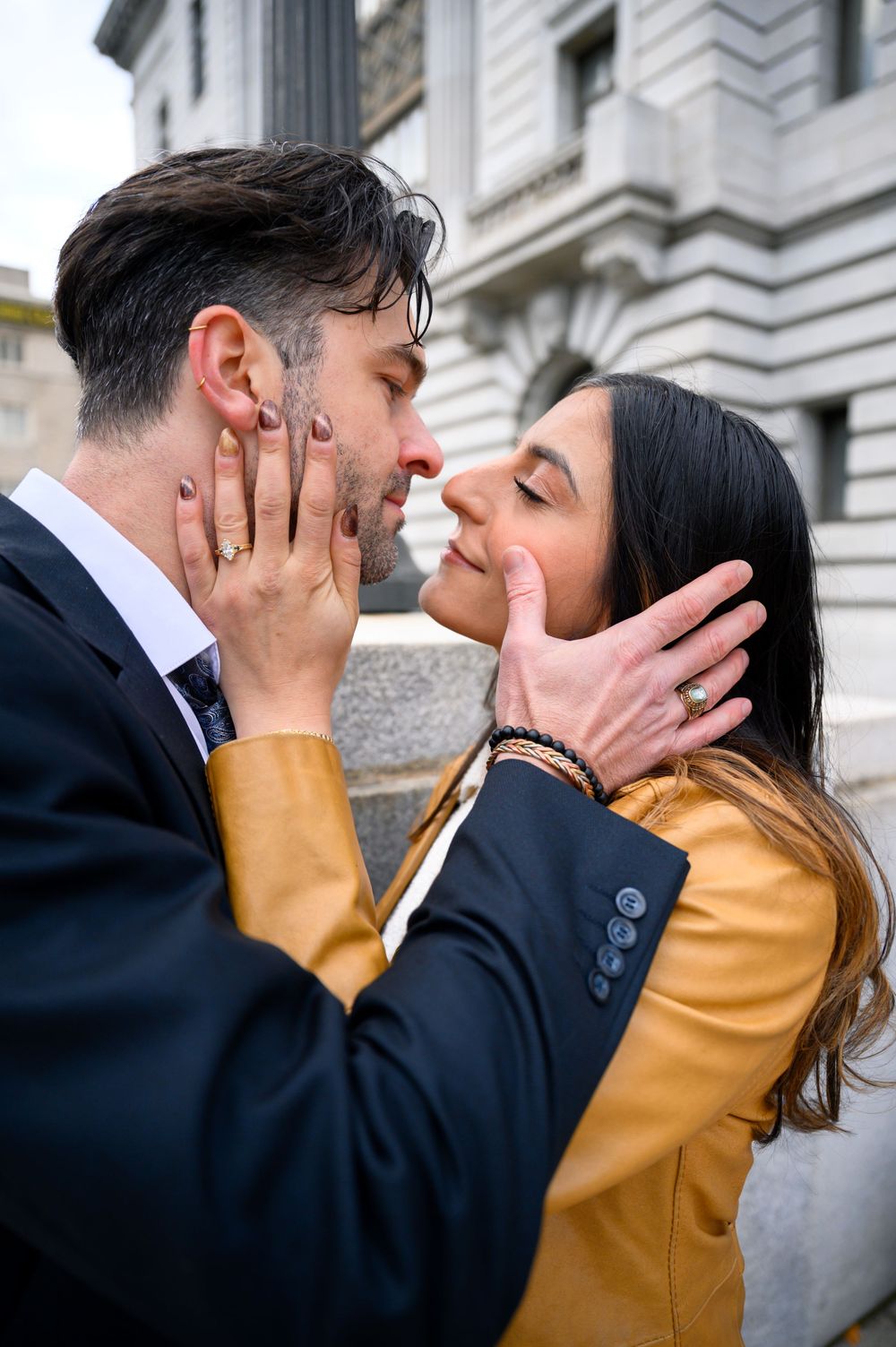 A couple in formal attire share a romantic kiss sequence against an elegant stone building exterior.