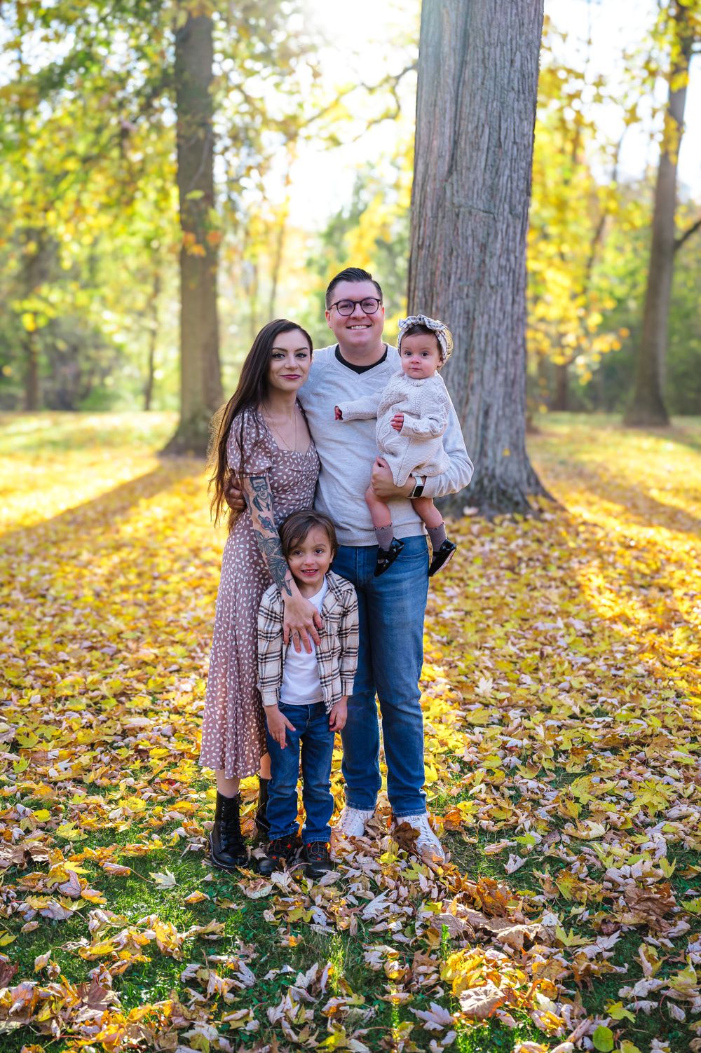 A family enjoys an autumn photo session among fallen leaves in a sunlit wooded area.
